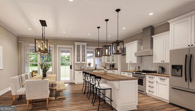 kitchen featuring butcher block counters, stainless steel range oven, fridge with ice dispenser, wall chimney exhaust hood, and an island with sink