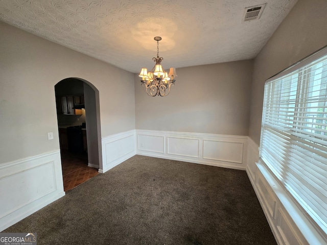 spare room featuring arched walkways, dark colored carpet, visible vents, a textured ceiling, and a chandelier