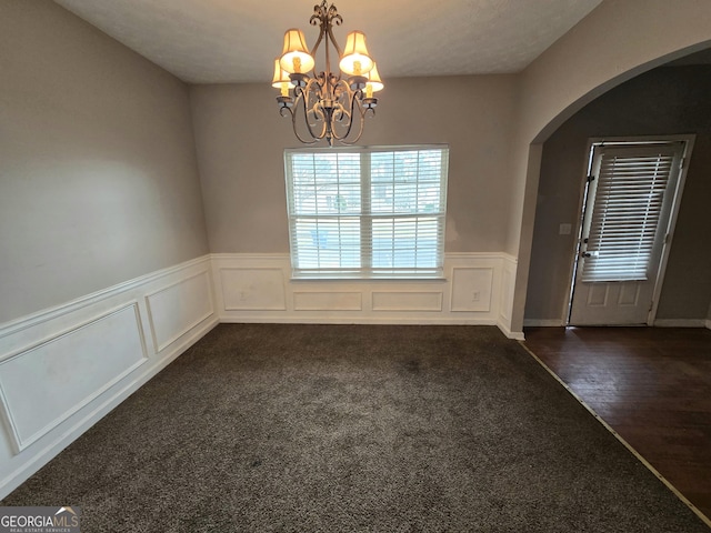 unfurnished dining area featuring arched walkways, wainscoting, dark carpet, dark wood finished floors, and an inviting chandelier