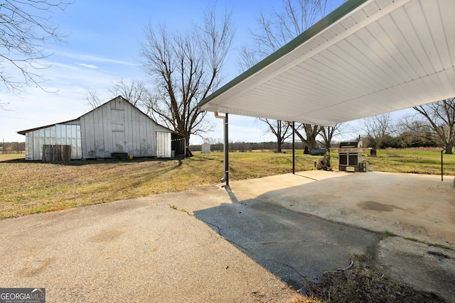 view of patio with driveway, an outdoor structure, a barn, and a detached carport