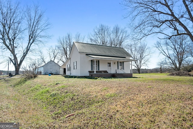 view of front of property featuring a porch, a front yard, metal roof, and an outbuilding