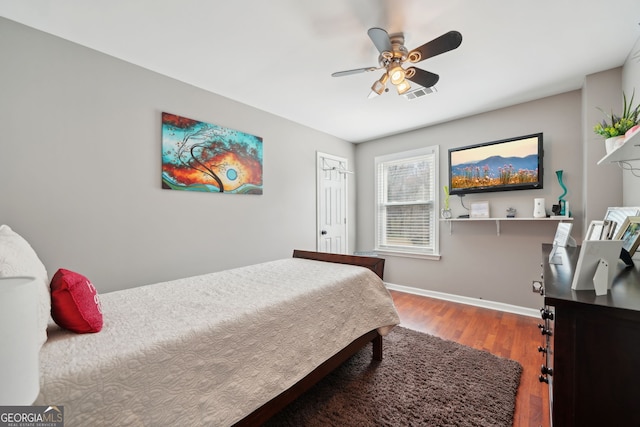 bedroom with ceiling fan, wood finished floors, visible vents, baseboards, and a closet