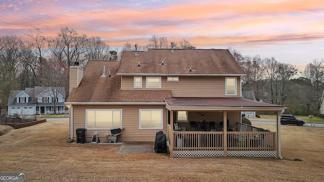 back of property at dusk featuring covered porch, a chimney, and a lawn