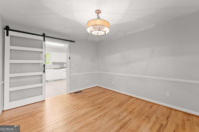 unfurnished dining area with visible vents, light wood-style flooring, a textured ceiling, and a barn door