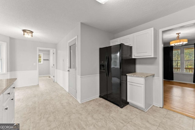 kitchen with a wainscoted wall, black refrigerator with ice dispenser, light stone counters, and white cabinets