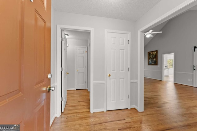 hallway featuring a textured ceiling, vaulted ceiling, light wood-type flooring, and baseboards