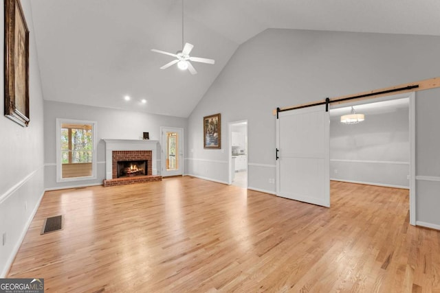 unfurnished living room featuring ceiling fan, a barn door, light wood-style flooring, visible vents, and a brick fireplace