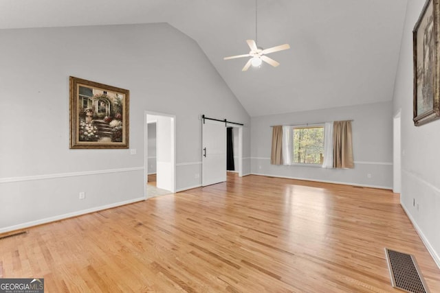 unfurnished living room featuring a barn door, visible vents, light wood-style flooring, and a ceiling fan