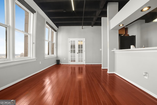 empty room featuring baseboards, beamed ceiling, hardwood / wood-style floors, and french doors