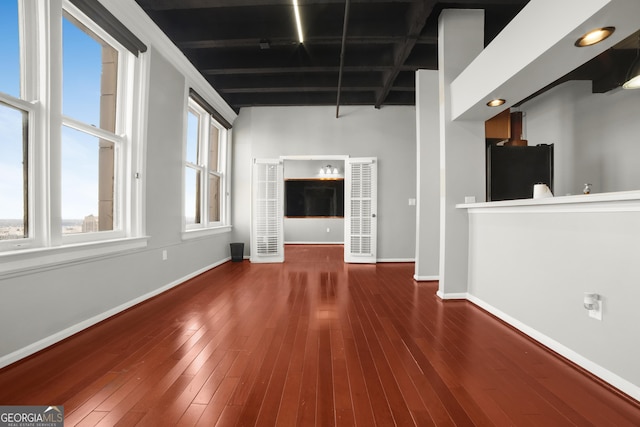 unfurnished living room featuring wood-type flooring, beamed ceiling, and baseboards