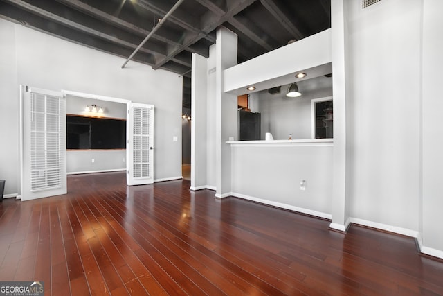 unfurnished living room featuring wood-type flooring, beamed ceiling, a towering ceiling, and baseboards