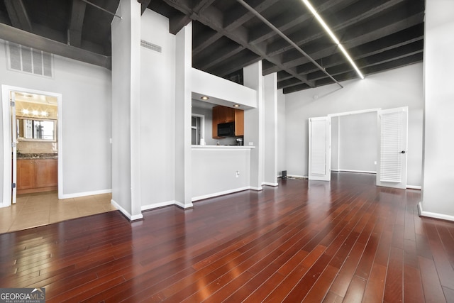 unfurnished living room with visible vents, a towering ceiling, baseboards, and wood finished floors