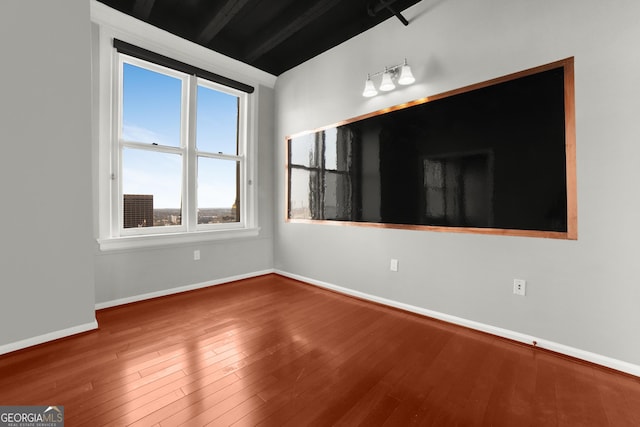 empty room featuring beam ceiling, baseboards, and hardwood / wood-style flooring