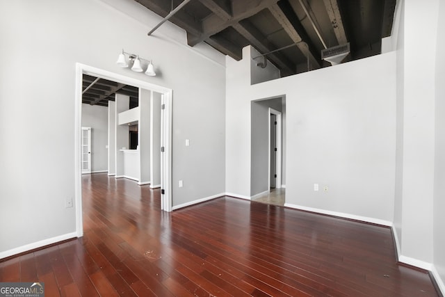 unfurnished room with beam ceiling, visible vents, a towering ceiling, hardwood / wood-style floors, and baseboards