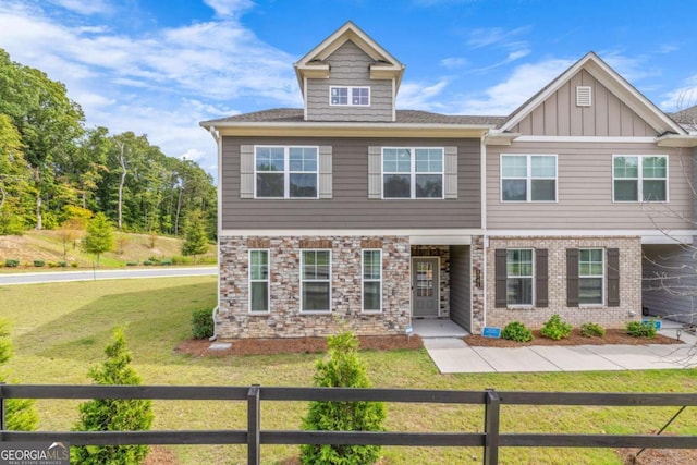 view of front of property with board and batten siding, brick siding, fence, and a front lawn