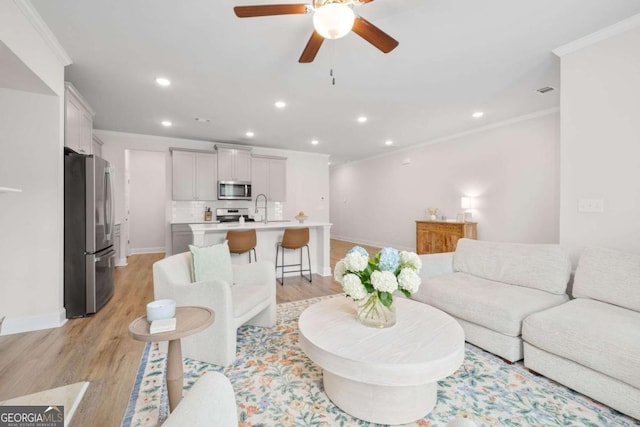 living room featuring light wood-style floors, baseboards, ornamental molding, and recessed lighting