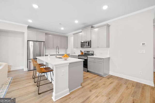 kitchen featuring crown molding, a breakfast bar area, gray cabinets, appliances with stainless steel finishes, and light wood-type flooring