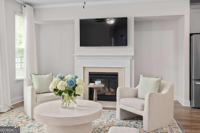 living area with ornamental molding, wood finished floors, a high end fireplace, and baseboards