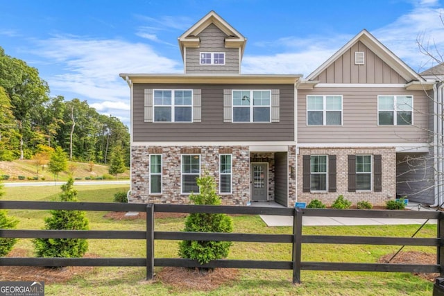 view of front of home featuring brick siding, board and batten siding, a front yard, and a fenced front yard