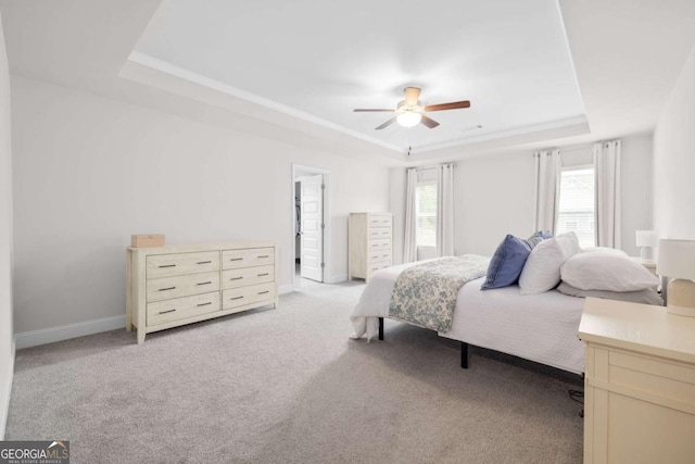 bedroom featuring baseboards, a tray ceiling, a ceiling fan, and light colored carpet