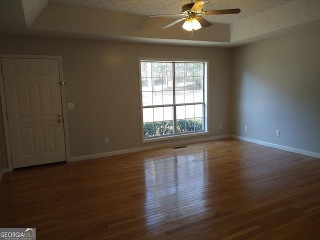 unfurnished room featuring ceiling fan, visible vents, baseboards, wood-type flooring, and a raised ceiling