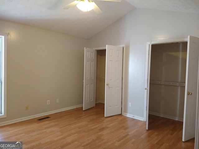 unfurnished bedroom with a walk in closet, lofted ceiling, visible vents, light wood-style flooring, and baseboards