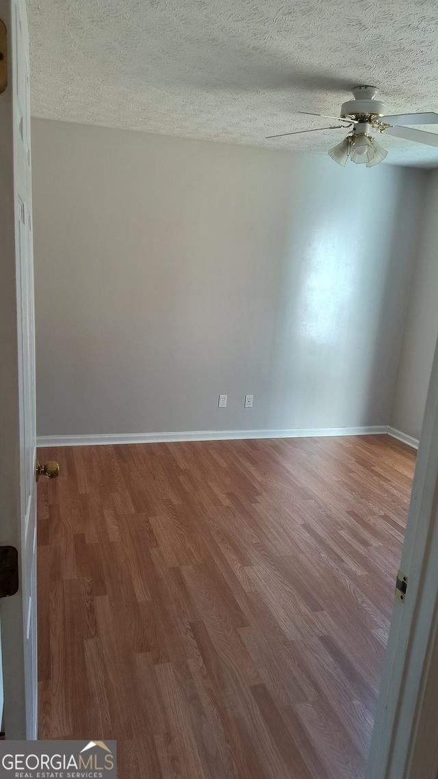 unfurnished room featuring a textured ceiling, ceiling fan, wood finished floors, and baseboards