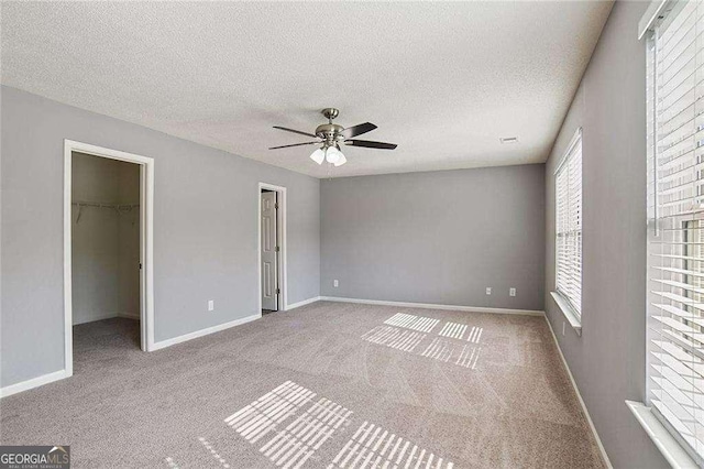 unfurnished bedroom with carpet floors, a walk in closet, a textured ceiling, and baseboards