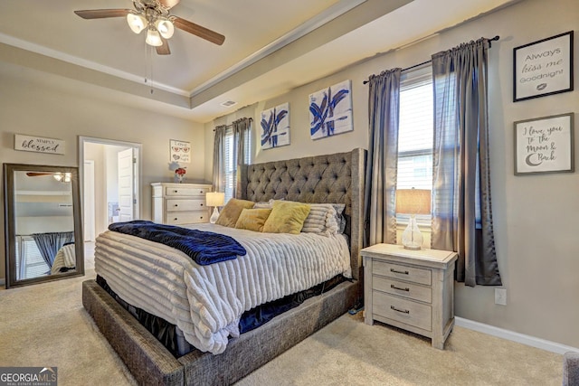 bedroom featuring light carpet, baseboards, a tray ceiling, and ceiling fan