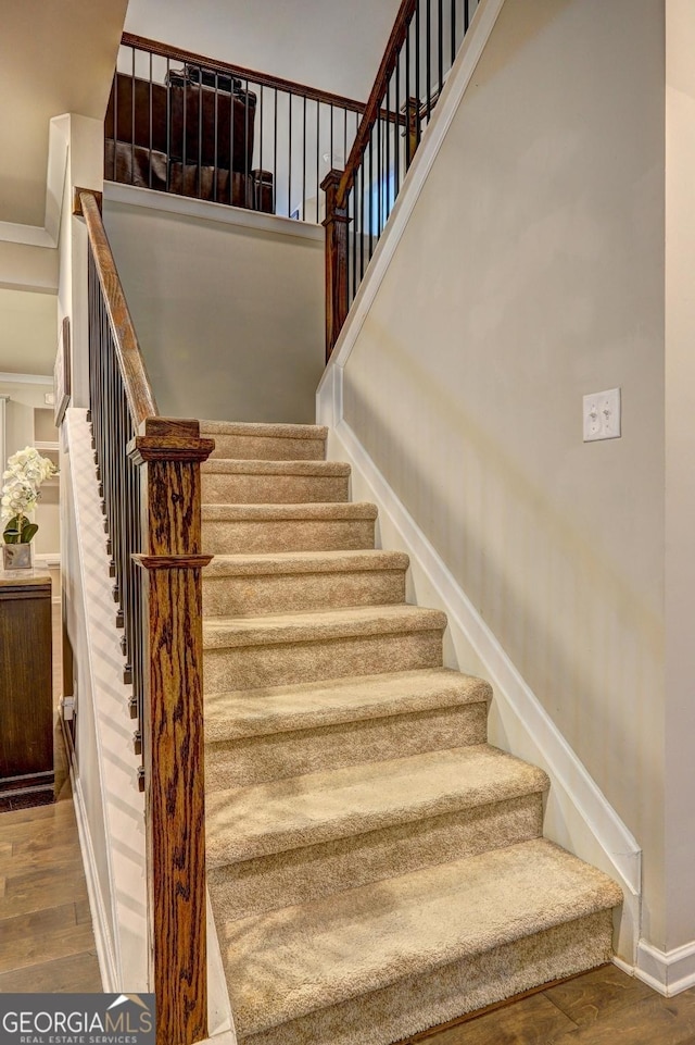 staircase with a high ceiling, wood finished floors, and baseboards