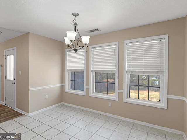 unfurnished dining area with a chandelier, a textured ceiling, visible vents, and baseboards