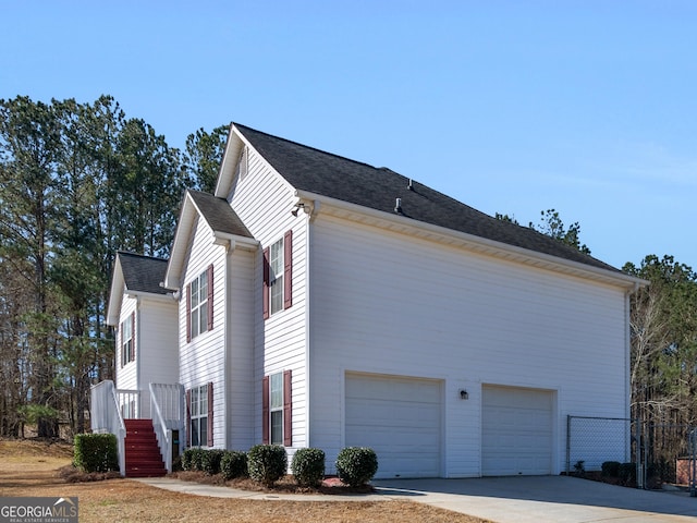 view of side of property with a garage, stairs, concrete driveway, and roof with shingles