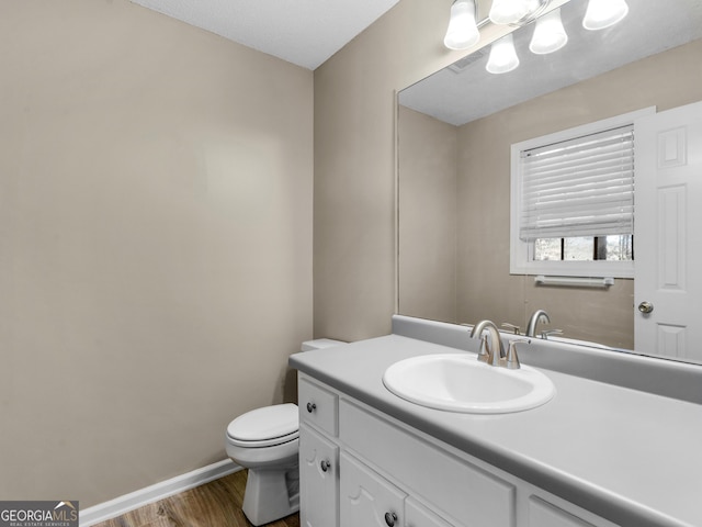 bathroom with toilet, wood finished floors, visible vents, vanity, and baseboards