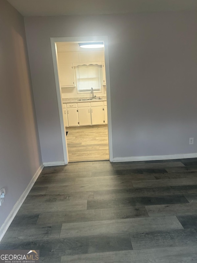 empty room with baseboards, dark wood-type flooring, and a sink