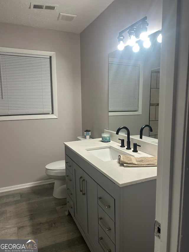 half bath with baseboards, visible vents, toilet, wood finished floors, and vanity