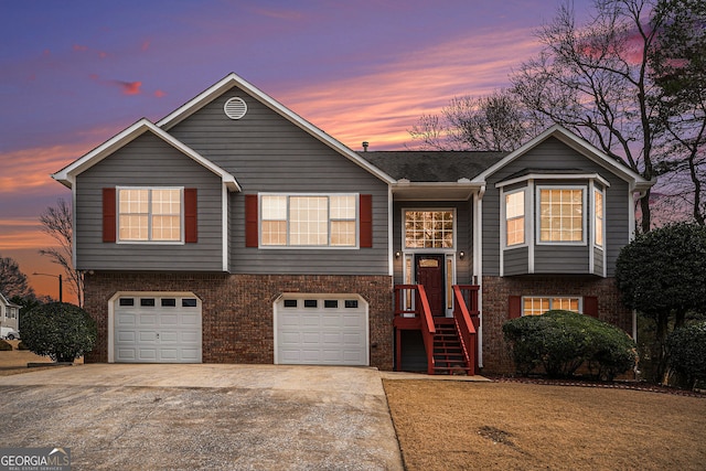 raised ranch featuring brick siding, an attached garage, and driveway