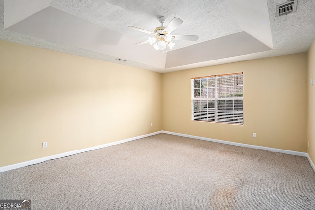 carpeted empty room featuring a ceiling fan, a textured ceiling, a tray ceiling, baseboards, and visible vents