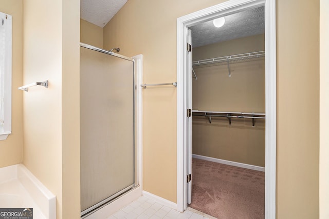bathroom with a spacious closet, baseboards, a textured ceiling, and a stall shower