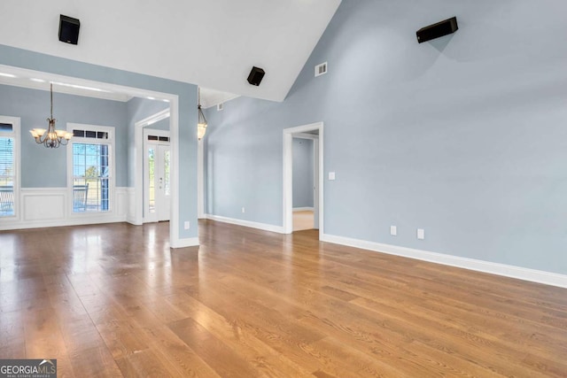 unfurnished living room with a chandelier, high vaulted ceiling, wood finished floors, visible vents, and wainscoting