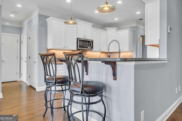 kitchen featuring tasteful backsplash, white cabinets, stainless steel microwave, a breakfast bar, and wood finished floors