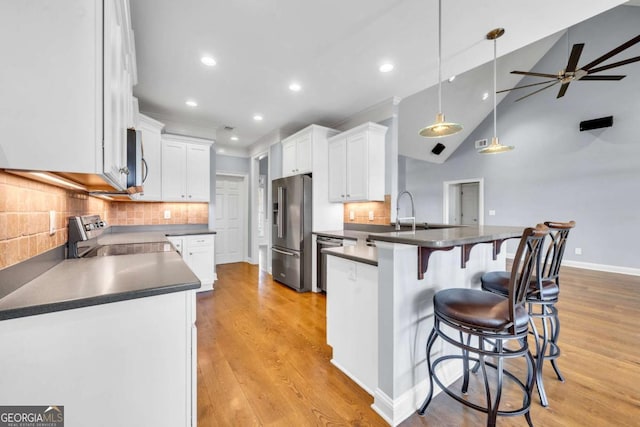 kitchen with a peninsula, appliances with stainless steel finishes, dark countertops, and white cabinetry