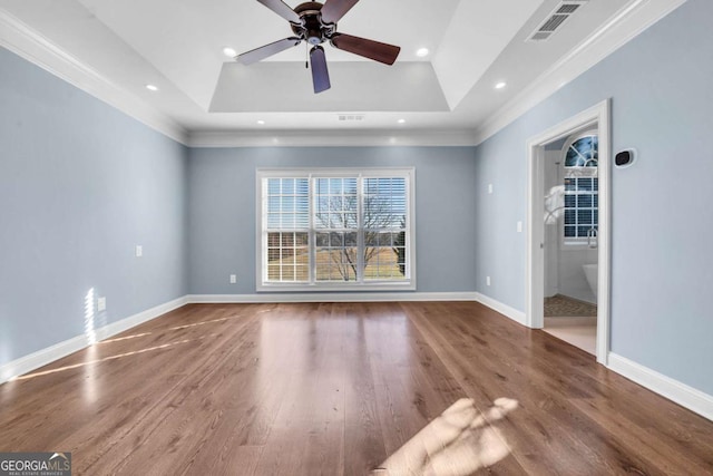 empty room featuring baseboards, visible vents, a raised ceiling, and wood finished floors