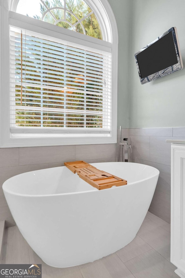 bathroom with a freestanding tub, tile patterned flooring, and tile walls