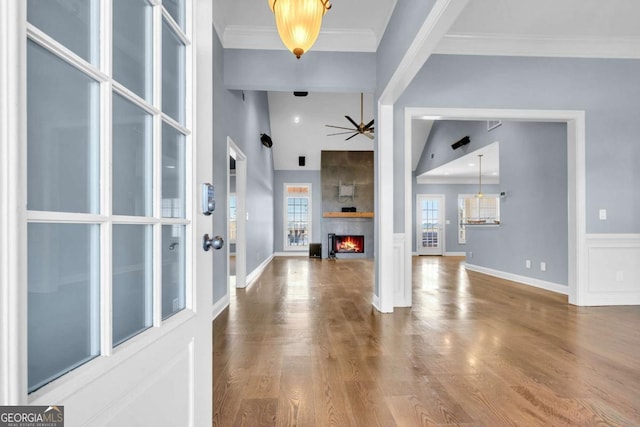 foyer with a large fireplace, ceiling fan, ornamental molding, and wood finished floors