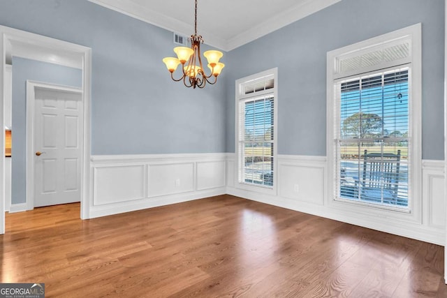 unfurnished dining area with a chandelier, wood finished floors, visible vents, ornamental molding, and wainscoting