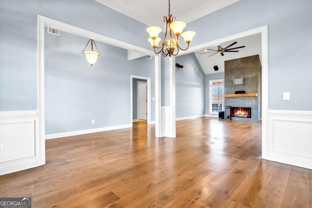 unfurnished living room with a decorative wall, a fireplace, wood finished floors, visible vents, and vaulted ceiling