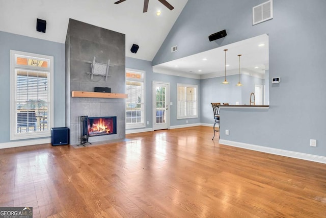 unfurnished living room with high vaulted ceiling, a tiled fireplace, visible vents, and wood finished floors