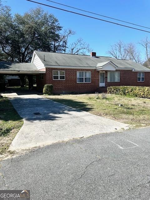 ranch-style house with driveway, brick siding, a chimney, and an attached carport