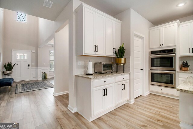 kitchen with light stone counters, stainless steel double oven, a toaster, visible vents, and light wood finished floors