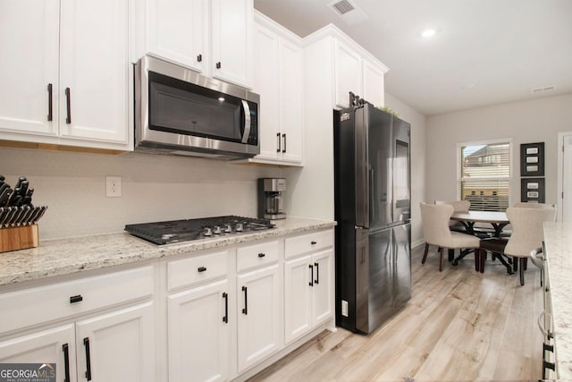 kitchen with visible vents, appliances with stainless steel finishes, light wood-style floors, white cabinets, and light stone countertops